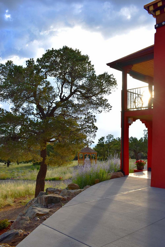 Patio and Garden at Sunset Adjacent to Red Building Patio beside red building balcony, tree, garden, gazebo, and grassy landscape at sunset.