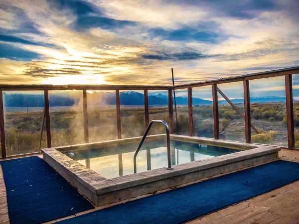 Outdoor Hot Tub with Mountain View at Sunrise Outdoor steaming hot tub on wooden deck with glass railing and mountain landscape at sunset. Colorado Meditation Retreat - Camino Wellness Center - Vova Kuperman