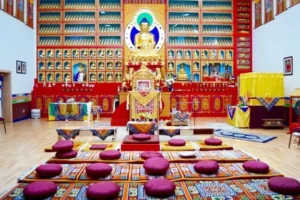 Interior of a Buddhist temple with a golden Buddha statue, prayer cushions, and ornate altar. Vajra Vidya Retreat Center - Crestone, Colorado - Meditation Retreat - 10 Day Meditation Retreat - Vova Kuperman